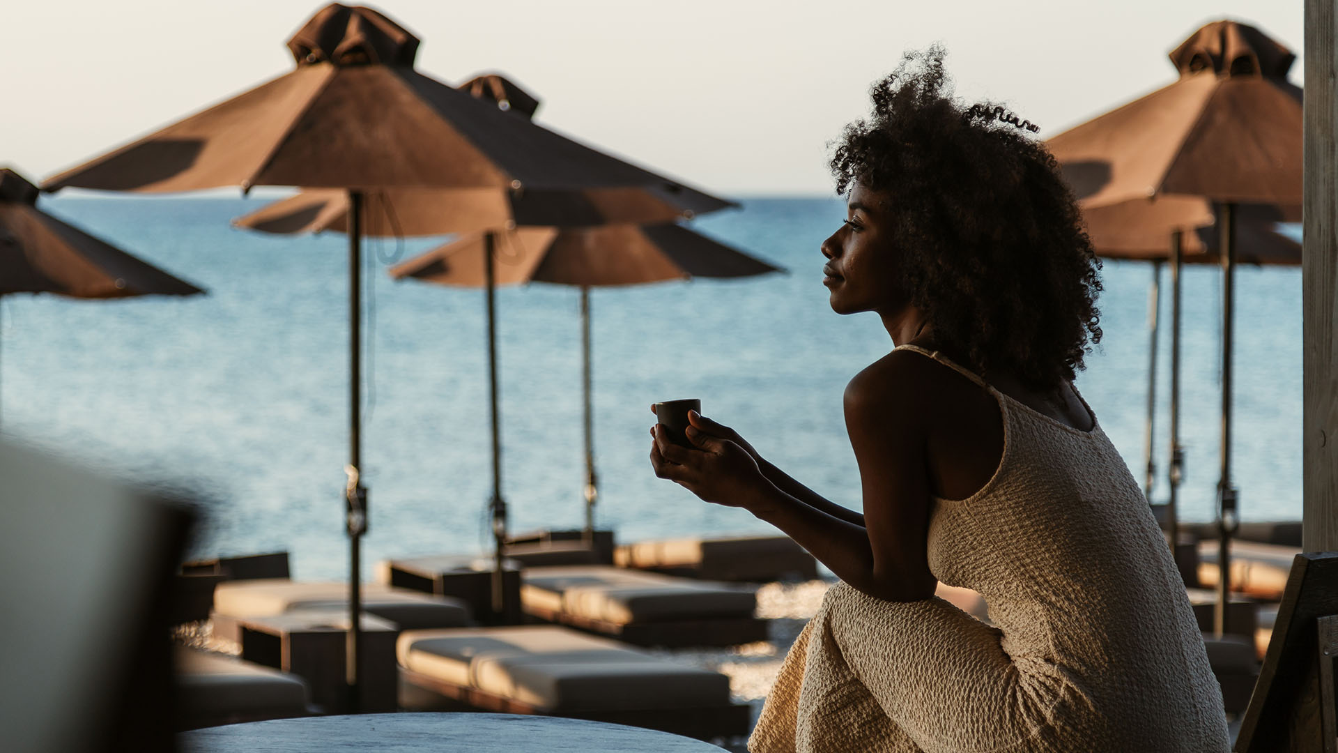 Woman at hotel beach during sunset with loungers and umbrellas, relaxed social environment